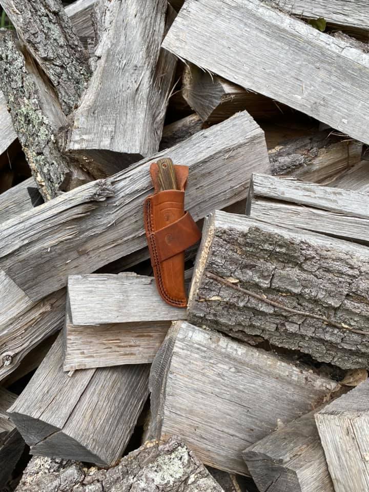 knife in leather case on wood pile